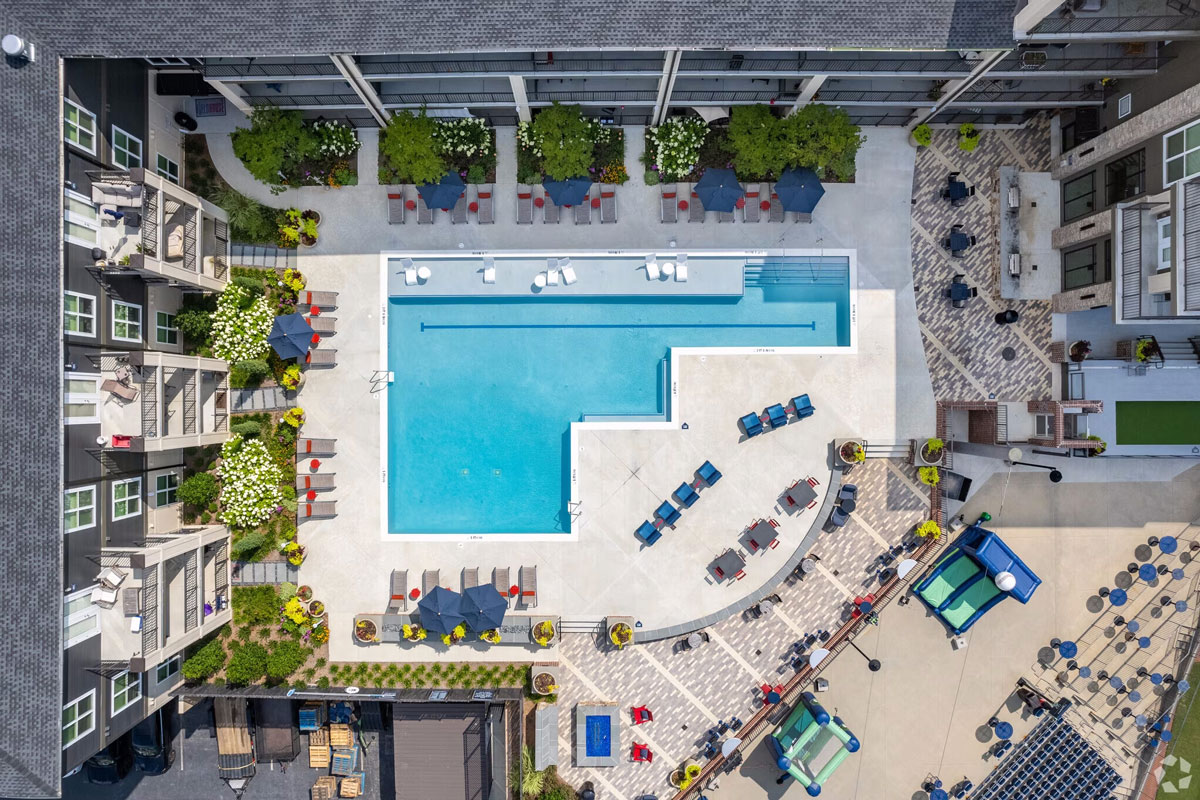 Aerial view of multifamily building and pool area with tables and chairs