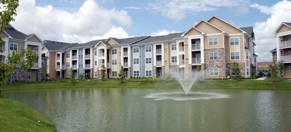 Photo of a pond with a fountain and a multifamily building in the background