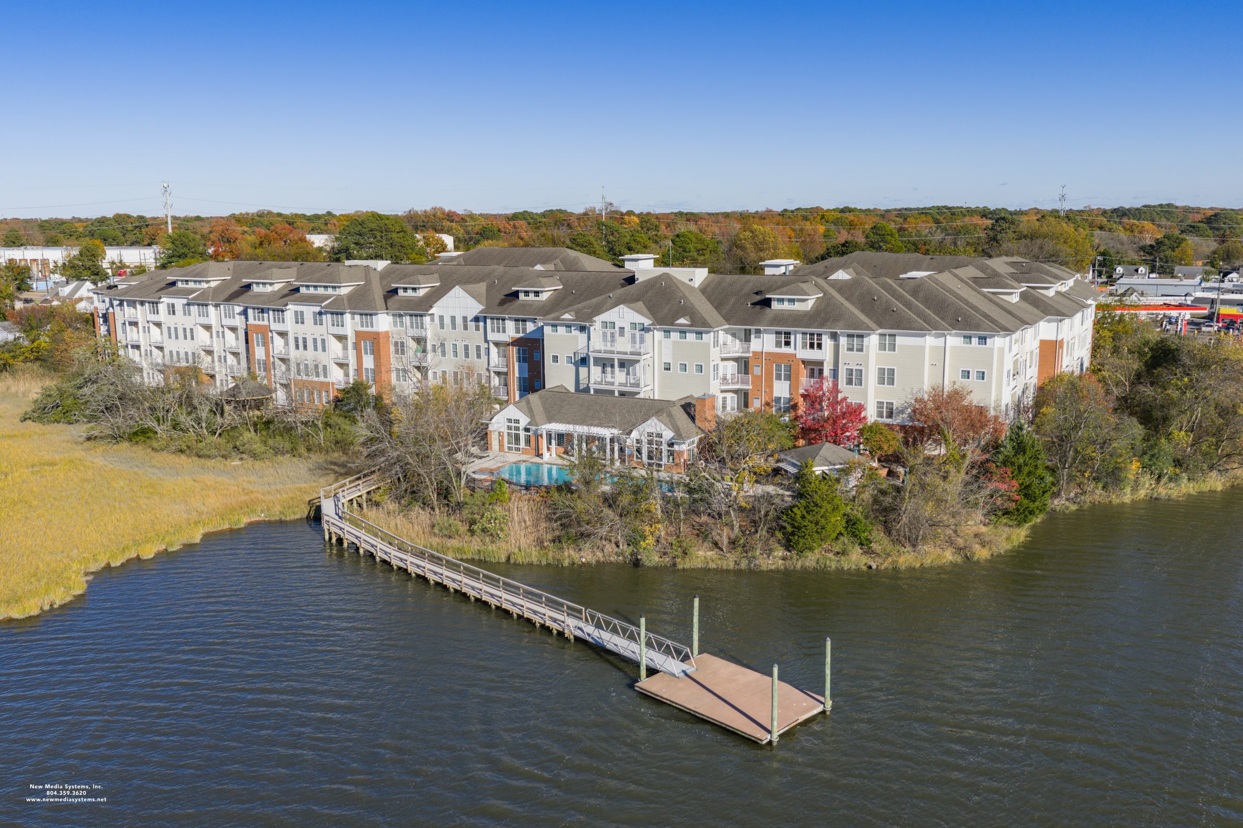 Aerial view of a multi-story residential building with a pool and dock situated by a body of water.