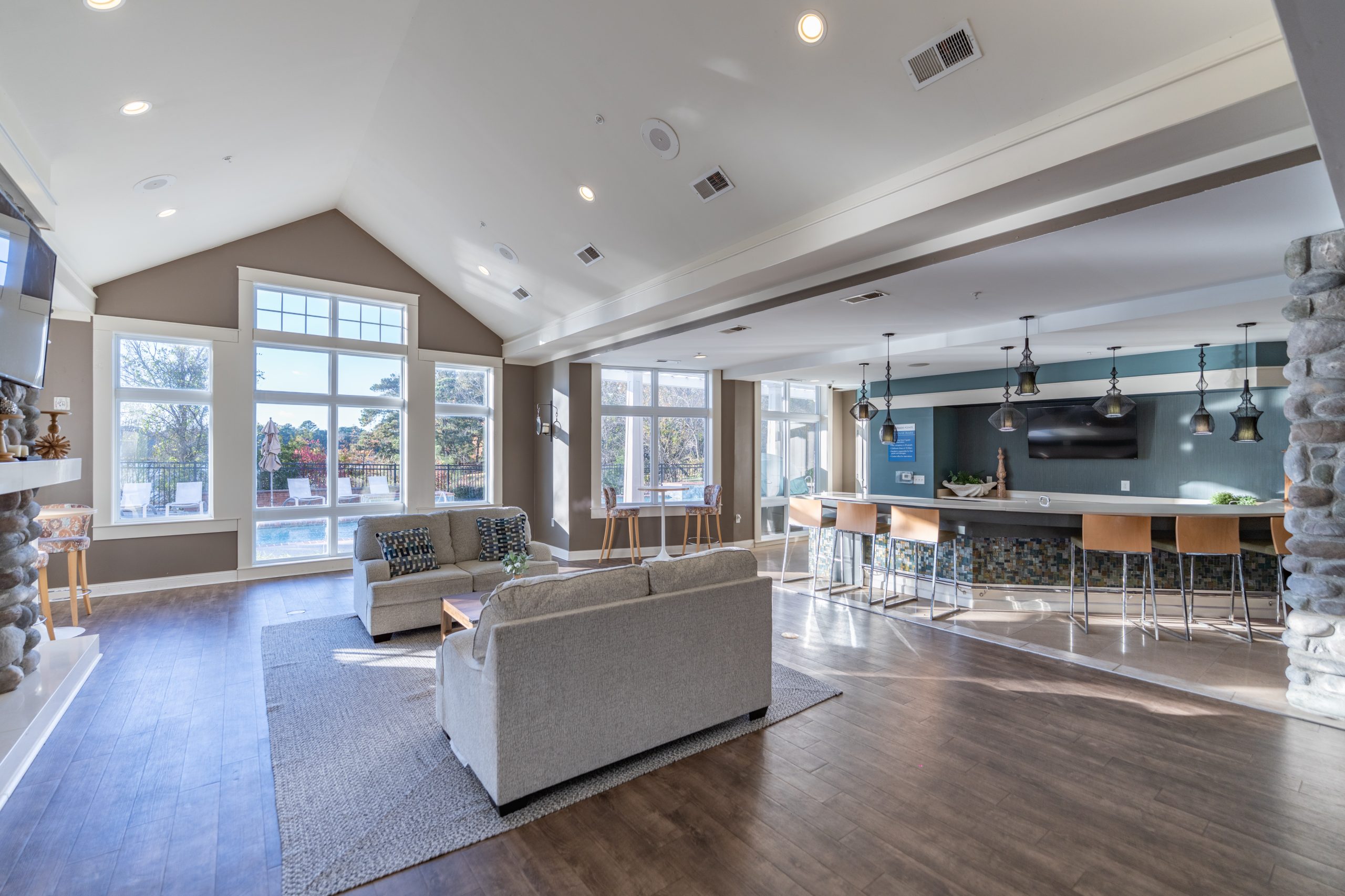 Interior of a modern lounge area featuring a light gray sofa, wooden coffee table, and a bar with high stools.
