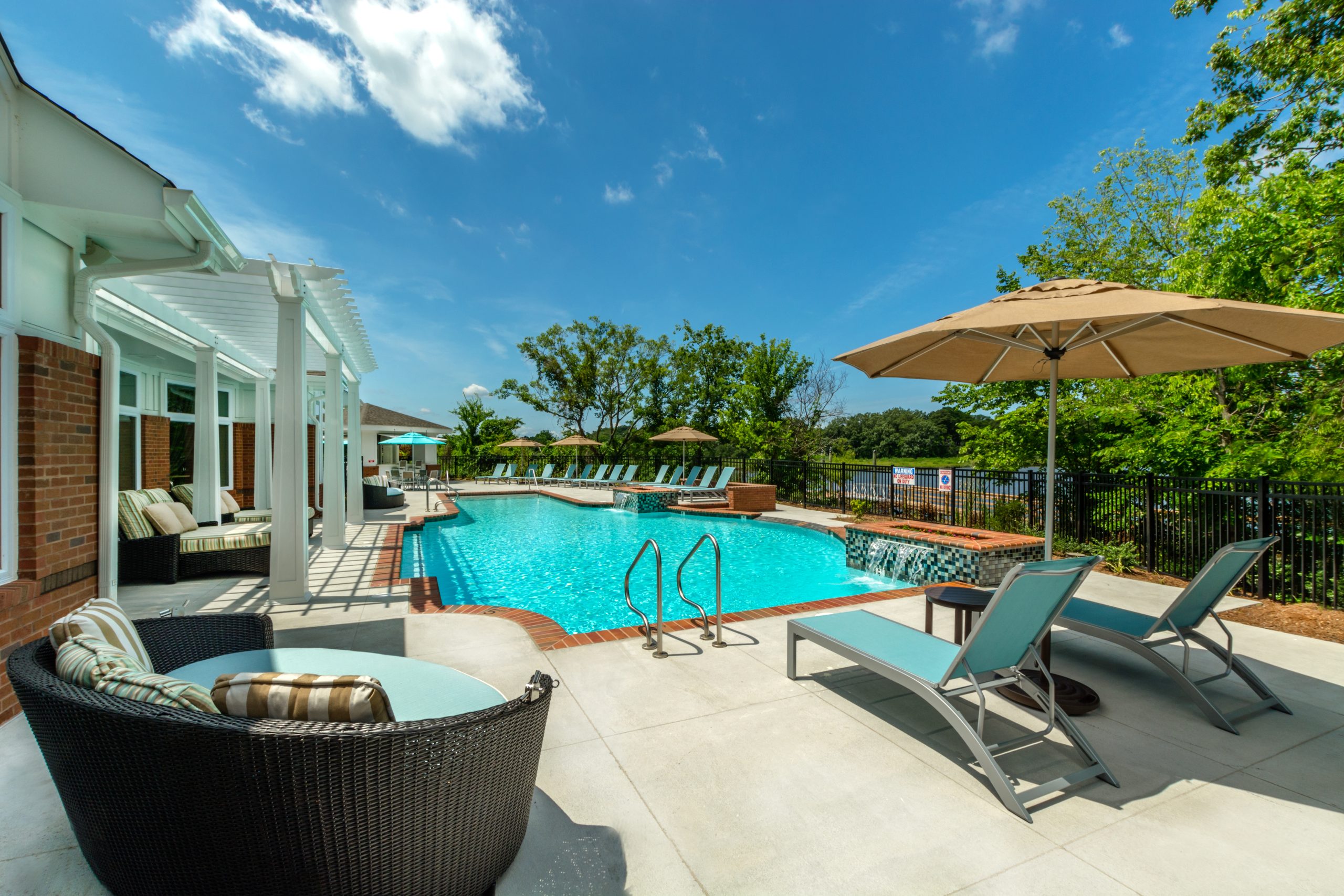 Swimming pool area with lounge chairs and umbrellas at Promenade Pointe Apartments, featuring a clear blue sky.